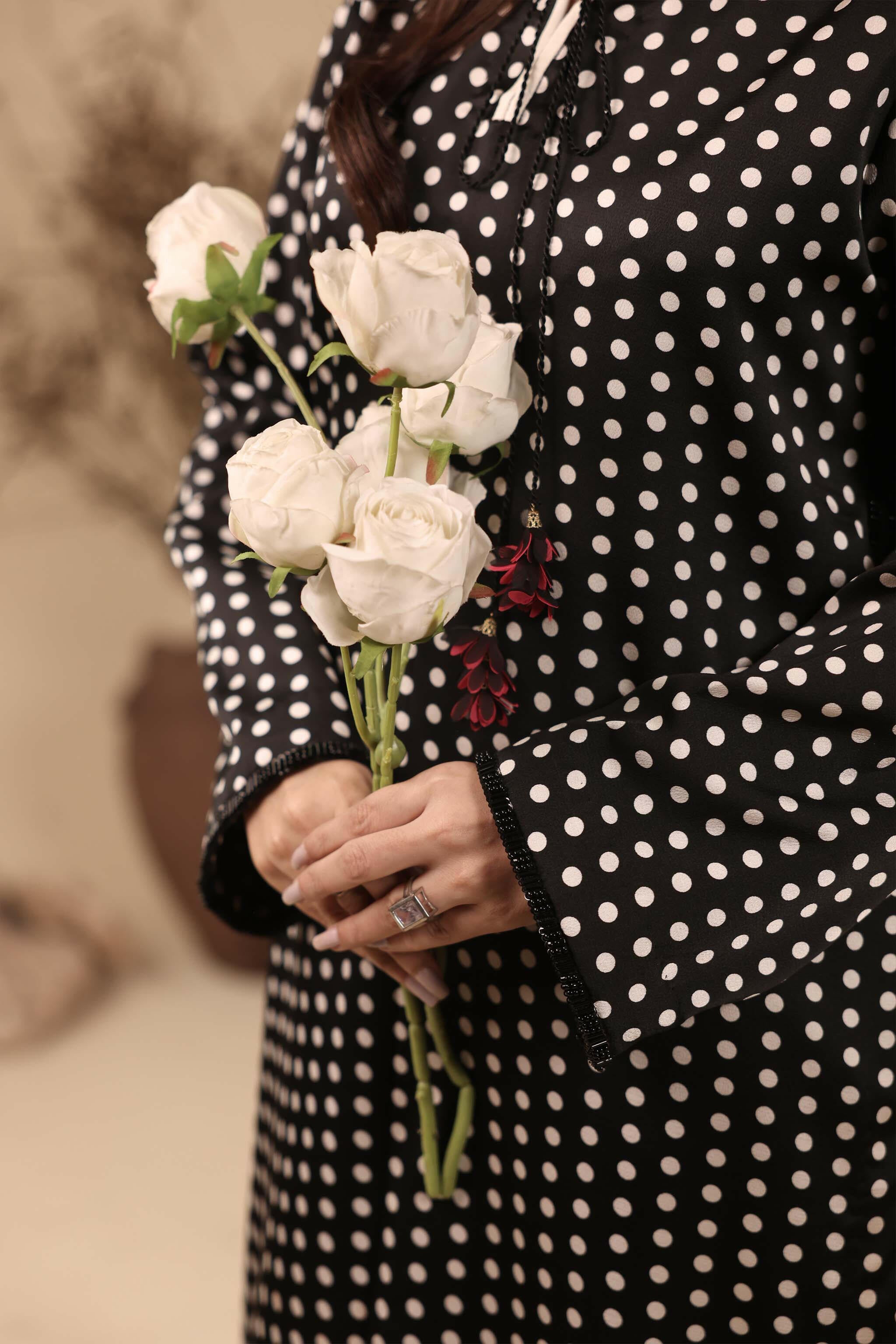 Black polka dot printed shirt in silk. It has embellished side slits and a tassel on the neckline. It is paired up with a white flared lower with black polka dots.